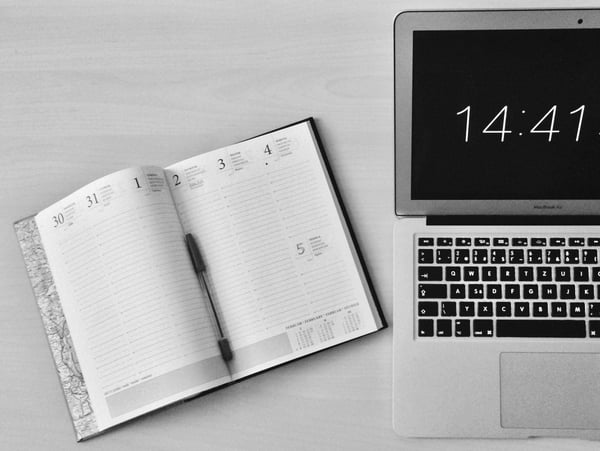 Open diary on desk next to MacBook with time on screen