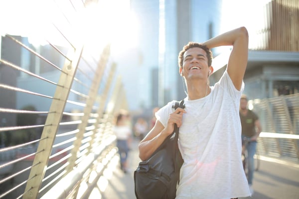 Smiling man walking with a bag over his shoulder outside in the sun